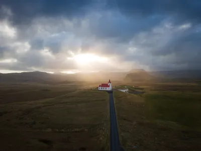 <p>A church with a red roof and steeple sticks out against the sprawling landscape as the sun pokes through the hazy clouds.</p>