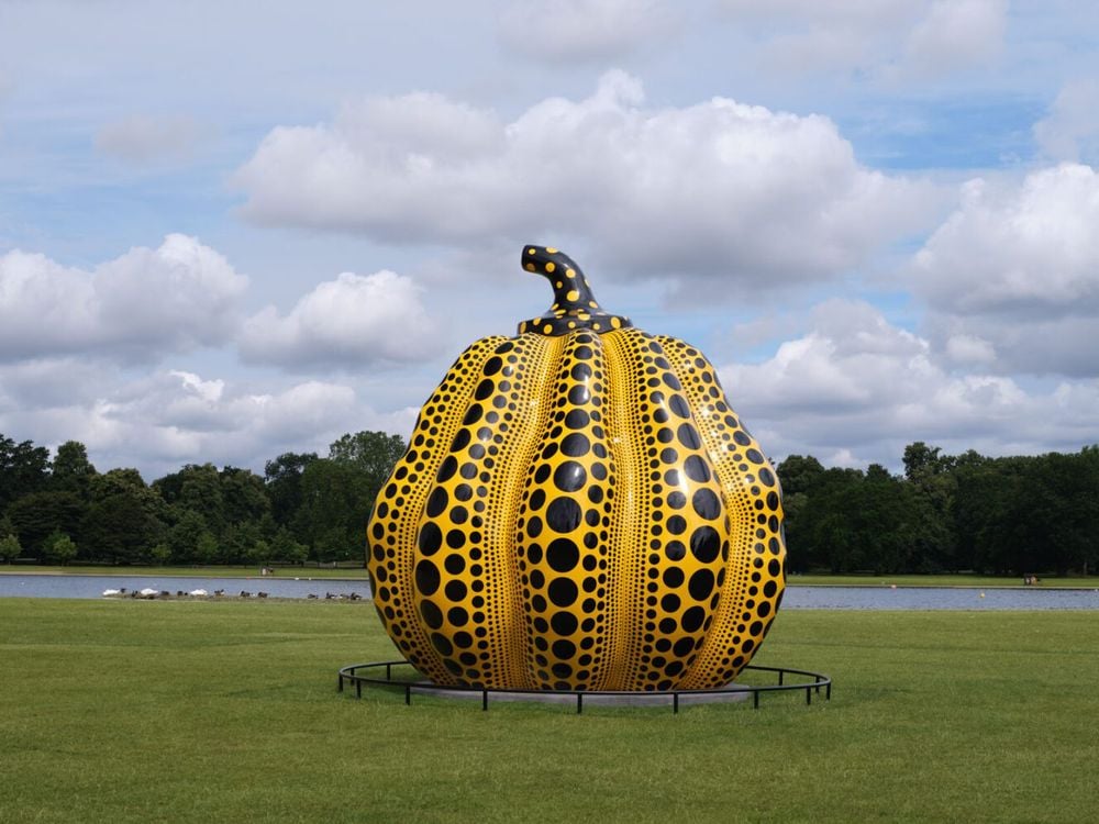 Large yellow pumpkin covered in black polka dots on a grassy area surrounded by trees