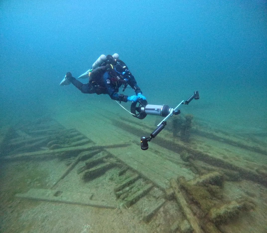 Underwater diver holding a device next to a shipwreck on the lake bed