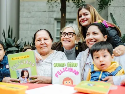 Woman smiles at the center of a group with young children and their mothers showcasing books they created