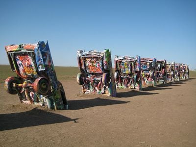 A group of 8 to 10 Cadillac cars half buried appear in a row with graffiti paint on them