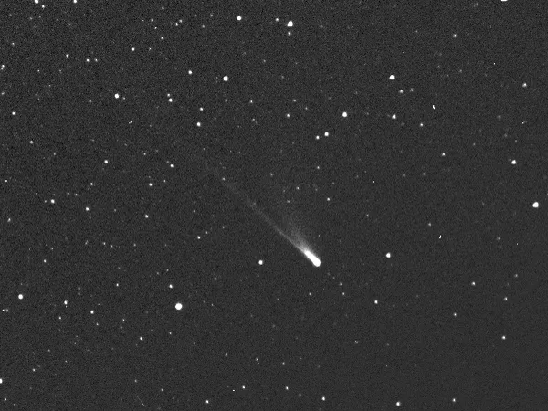 a comet streaks diagonally toward the bottom right of the image across a sky full of stars